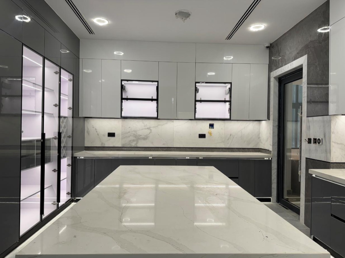 A large custom kitchen in grey and white gloss with a marble worktop island and backlit display cabinets